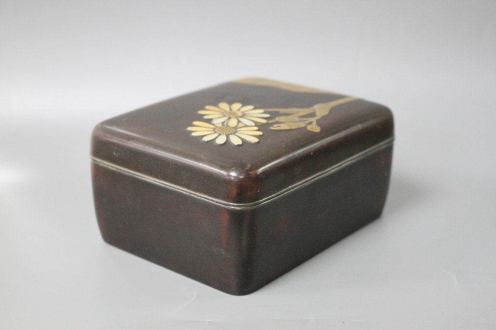 A Japanese Meiji period lacquer box, decorated with lotus leaves and flowers, with the petals inset with mother of pearl, silver rim an